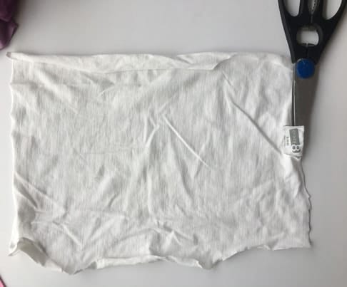 cut piece of white kid's shirt with a pair of scissors on top