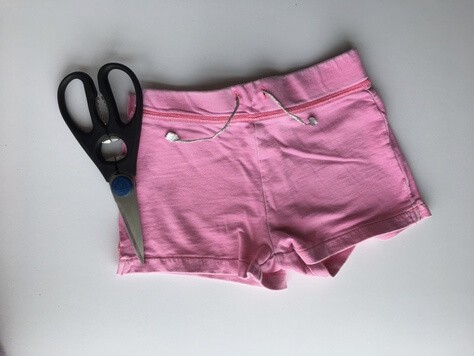 pair of pink shorts with a pair of scissors laying on top