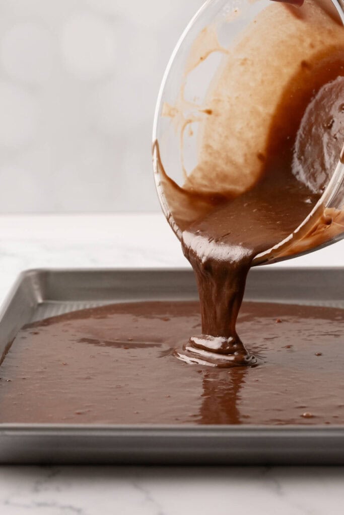 pouring chocolate sheet cake batter into a sheet pan