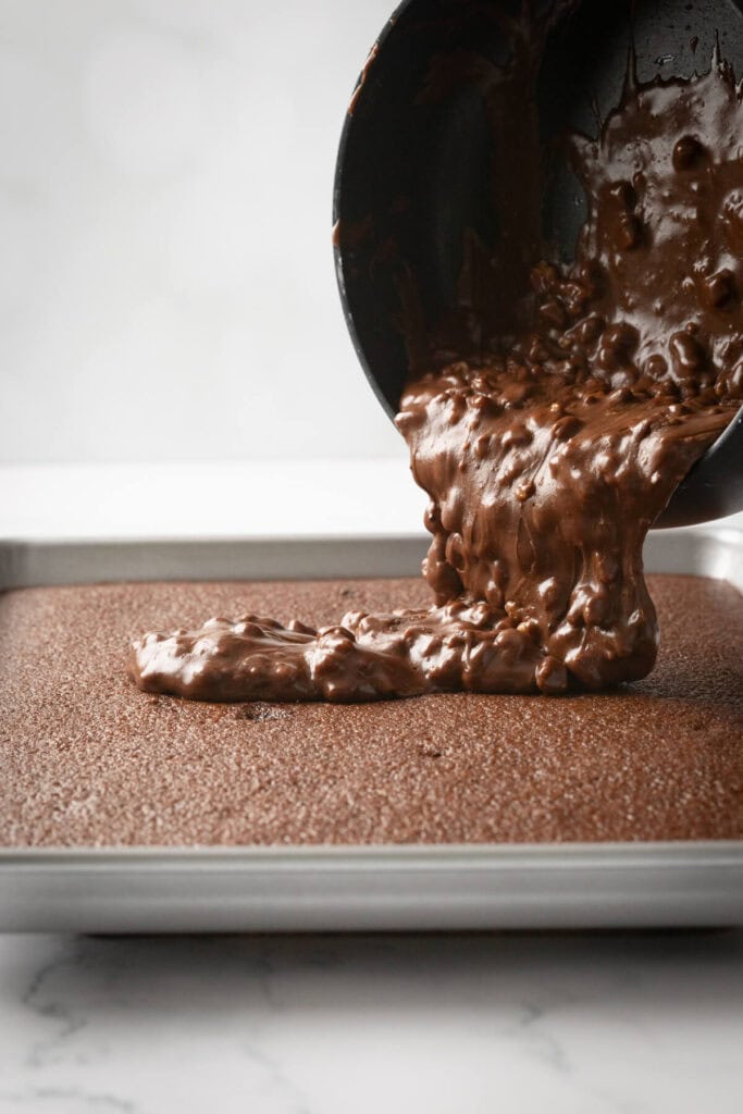 pouring chocolate frosting onto a sheet cake