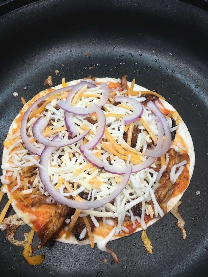 tortilla pizza being cooked in a skillet