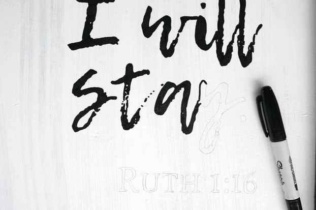 black Sharpie marker laying on white sign with outline of wording "I will stay" partially colored in