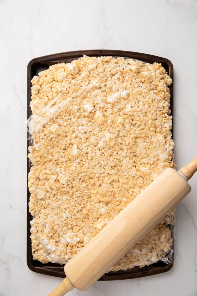 using a rolling pin to flattened cereal treats on a sheet tray