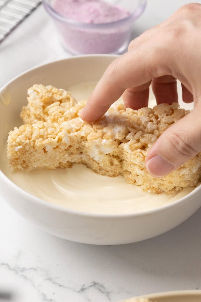 dipping a bunny shaped rice krispie treat in melted white chocolate