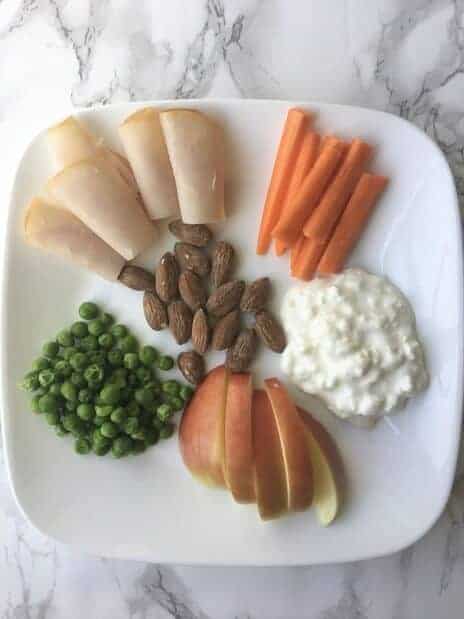 snack plate for kids with turkey rolls, almonds, carrots, cottage cheese, apple slices and peas
