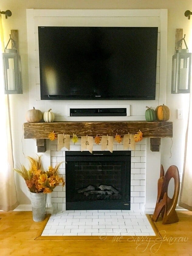 fireplace mantel decorated for fall with pumpkins and a fall burlap banner