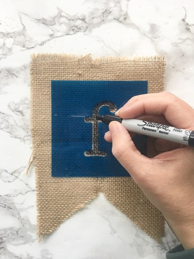 woman's handing using a stencil to color the letter f on to a burlap pennant