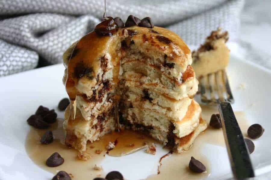 chocolate chip pancakes stacked up and covered in syrup with a large bite taken out of the side