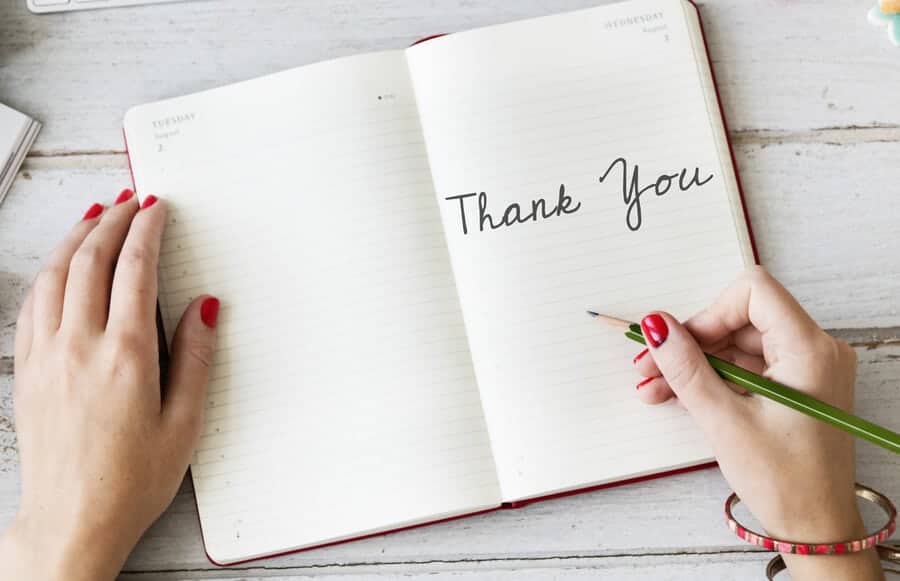 lady writing the words "Thank You" in a lined journal