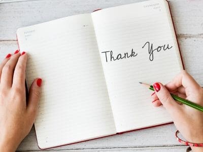 lady's hands writing the words "Thank You" in a journal