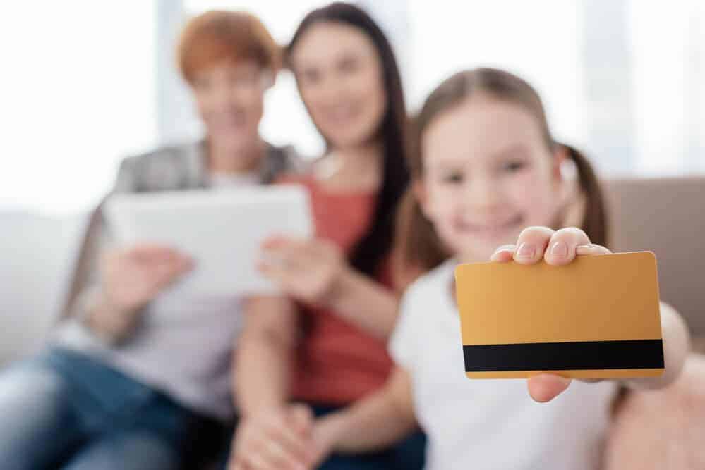 young girl holding debit cards for kids with 2 adults in the background