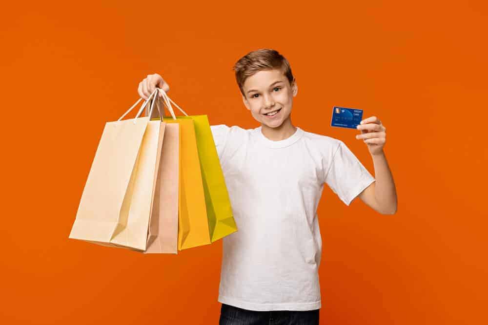 young boy holding debit cards for kids and shopping bags