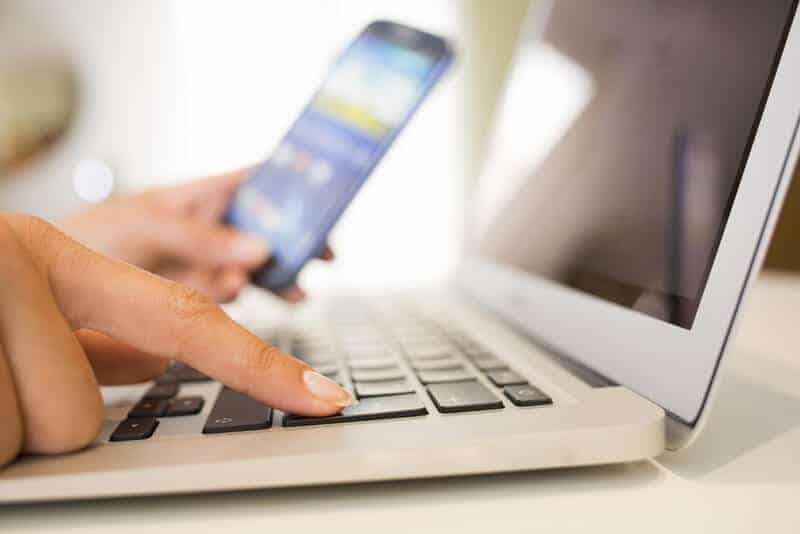 woman typing on a keyboard while holding a smart phone