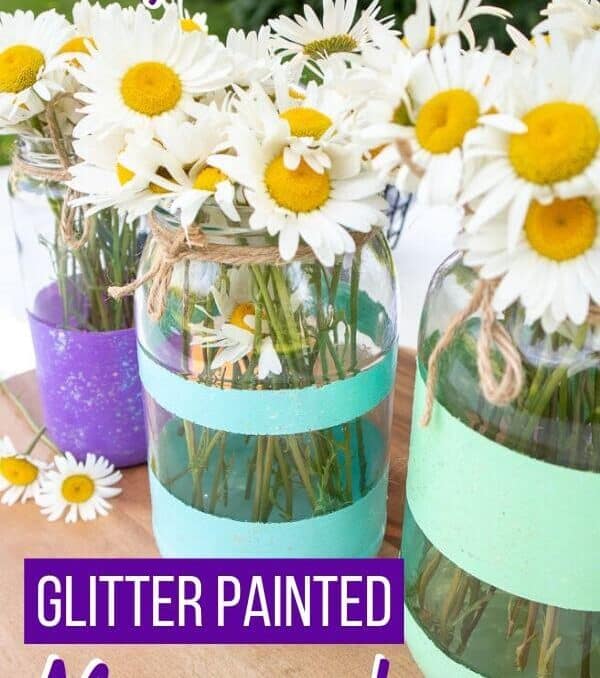 three painted mason jars with glitter stripes on a table with daisies in them