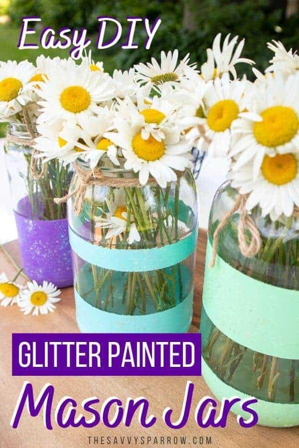 three painted mason jars with glitter stripes on a table with daisies in them