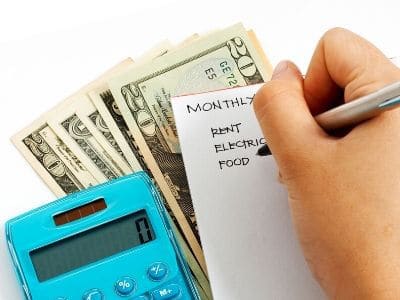 woman writing down monthly bills next to cash and calculator