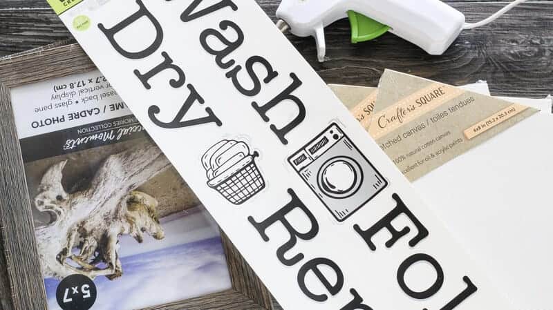 Dollar Tree laundry decals, picture frames, white art canvas, and hot glue gun on a table