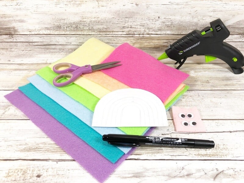 rainbow felt sheets, hot glue gun, rainbow template, scissors, and marker on a table
