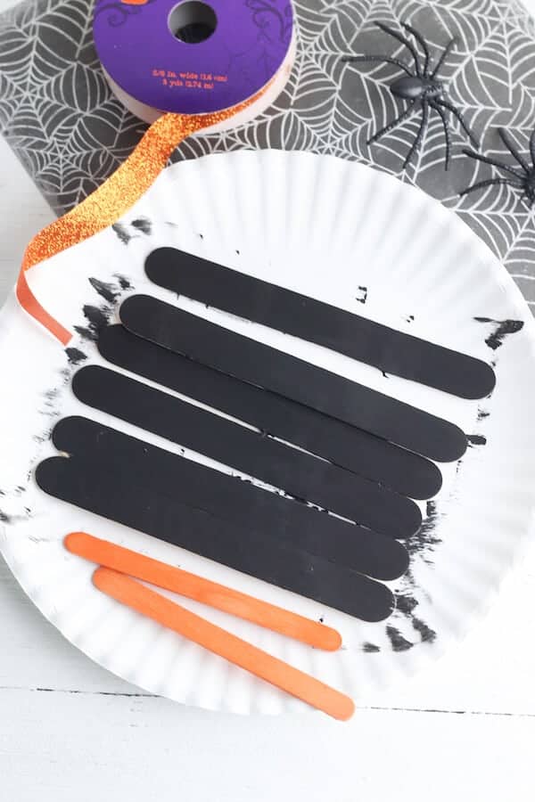 black and orange craft sticks on a paper plate