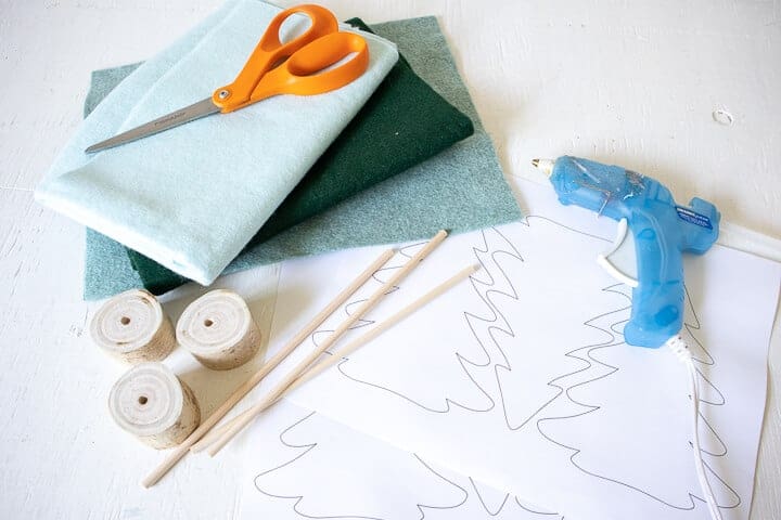 green felt sheets, wood dowels, wood stumps, glue gun, and scissors on a table