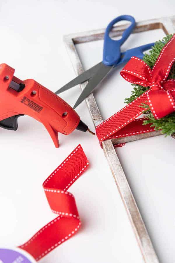 a hot glue gun being used to attach a wreath to a DIY fake window frame