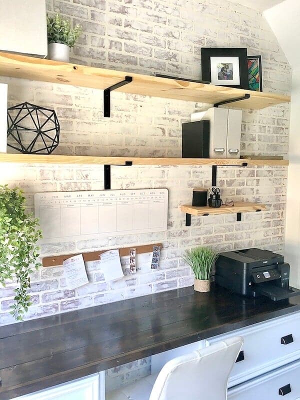 home office with open shelves and a faux brick accent wall