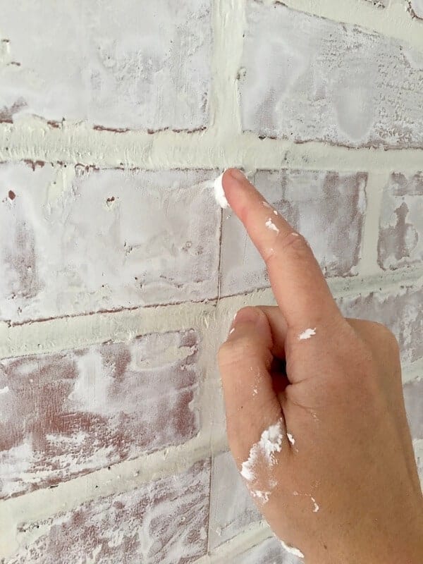 woman's finger smearing joint compound on a white brick wall