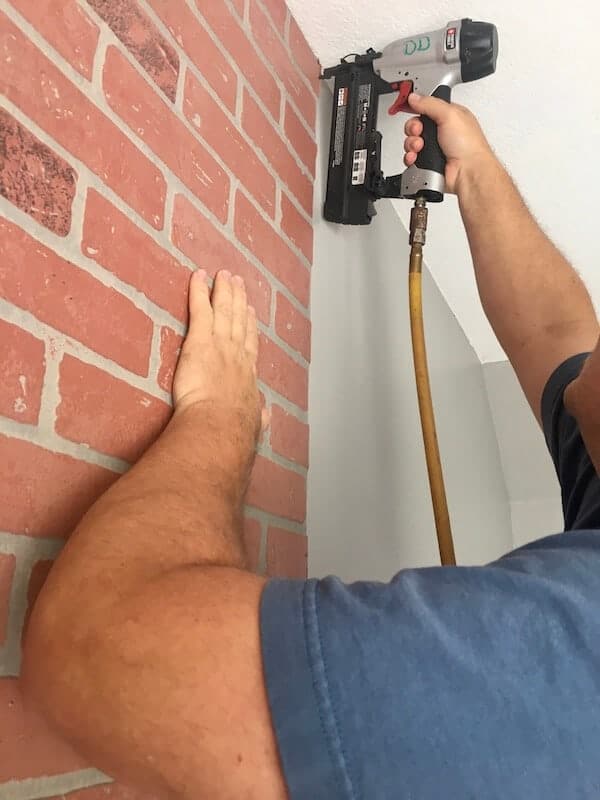 man using a nail gun on a faux brick wall panel