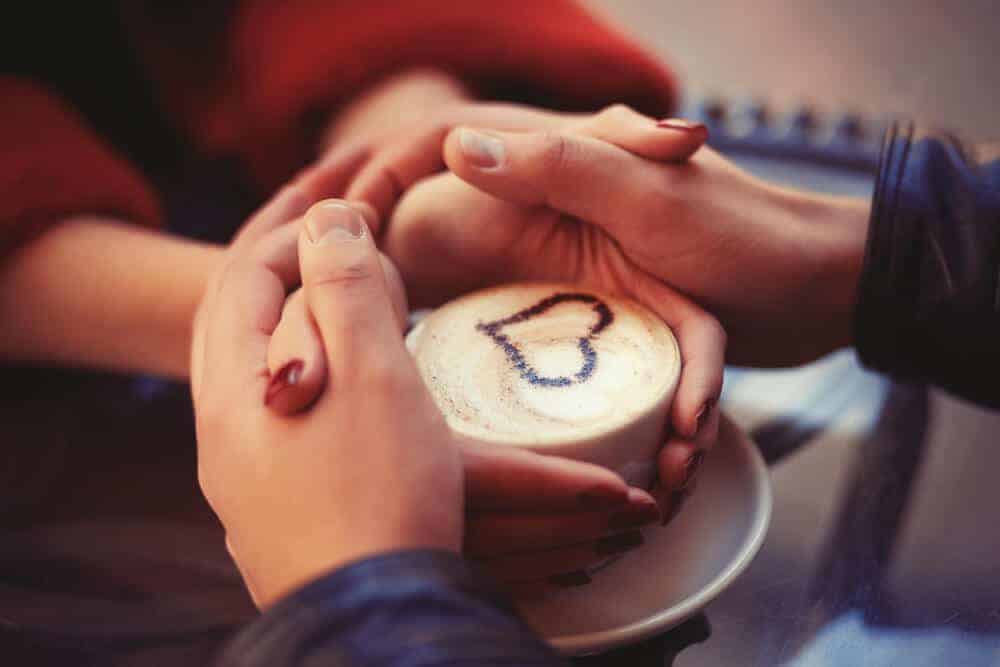 two peoples hands wrapped around a coffee cup