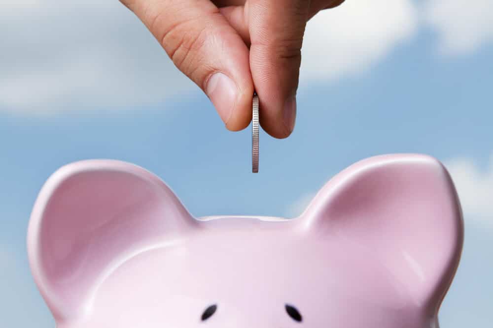 hand putting a coin into a piggy bank