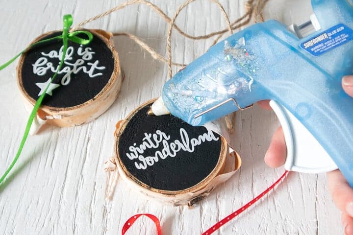 hot gluing a bow onto a wood slice ornament