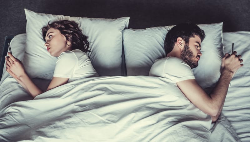 married couple laying in bed using cell phones