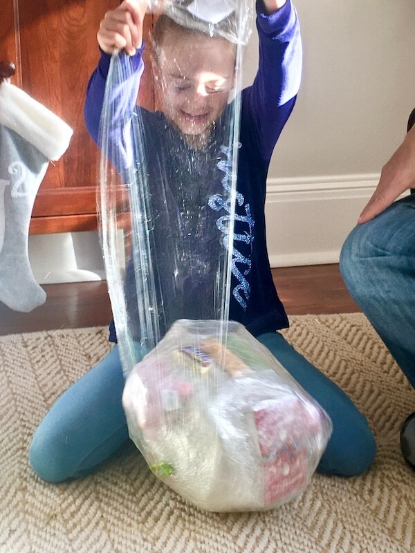 young girl opening a plastic wrap ball with prizes inside