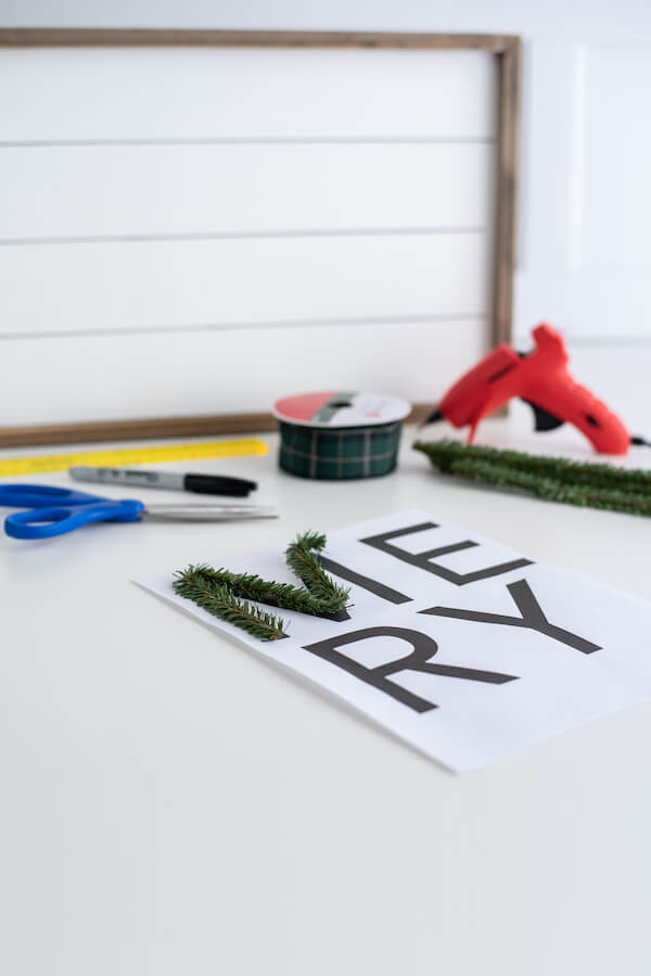 forming wired pine stems on a sign template that says Merry