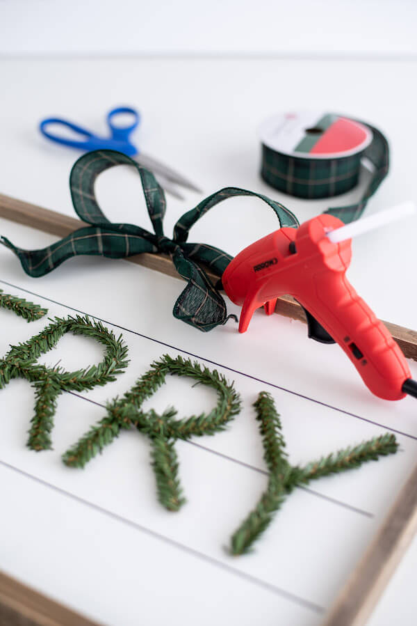 pine stem letters being hot glued on a wooden Christmas sign