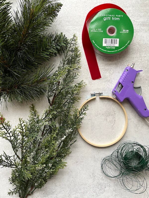 embroidery hoop, faux evergreen stems, hot glue gun, wire, and ribbon