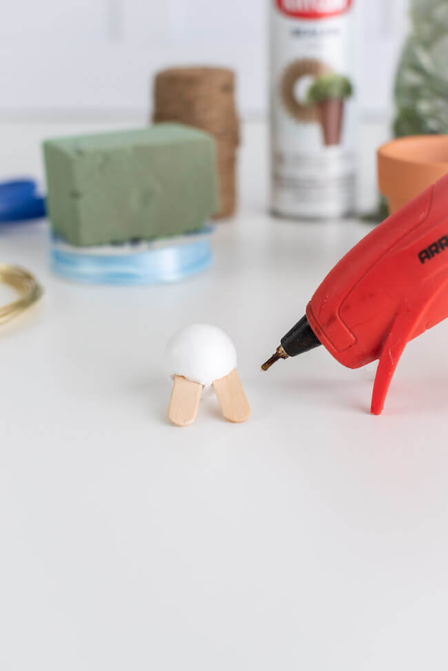 hot gluing popsicle sticks to a styrofoam ball to make a bunny head