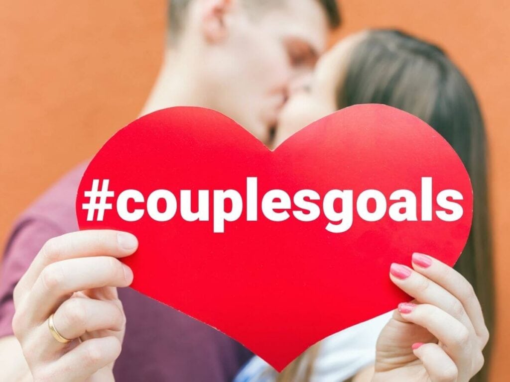 couple kissing holding a heart that says couples goals