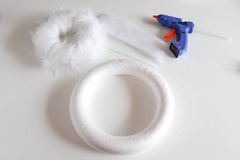 hot gluing white fur ribbon around a wreath form