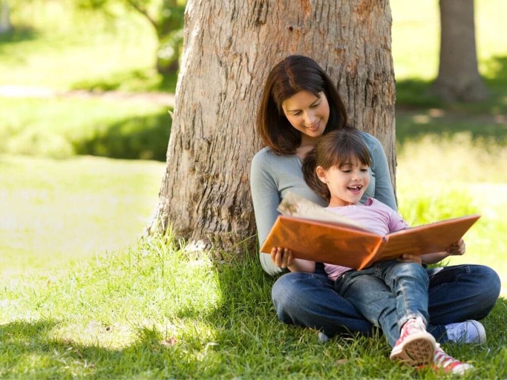 mother and daughter reading a book under a tree