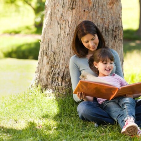 mother and daughter reading a book under a tree