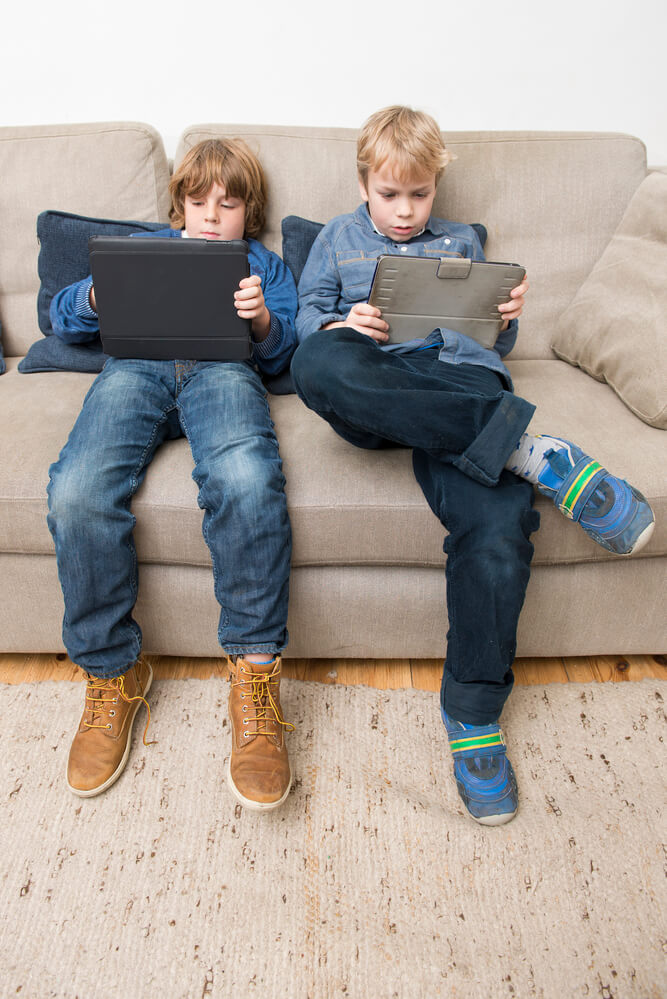two kids using tablets on a couch