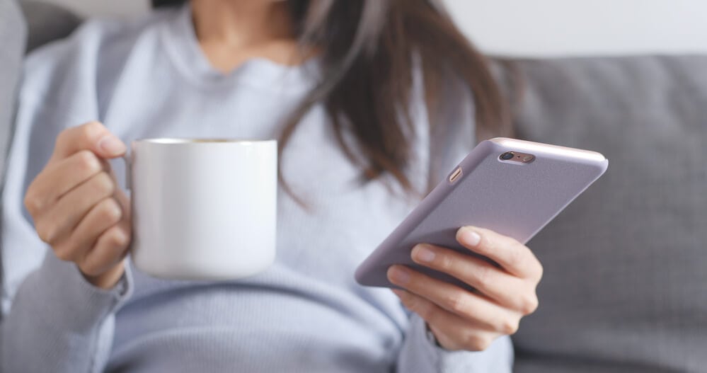 woman sending a good morning text message and holding coffee cup