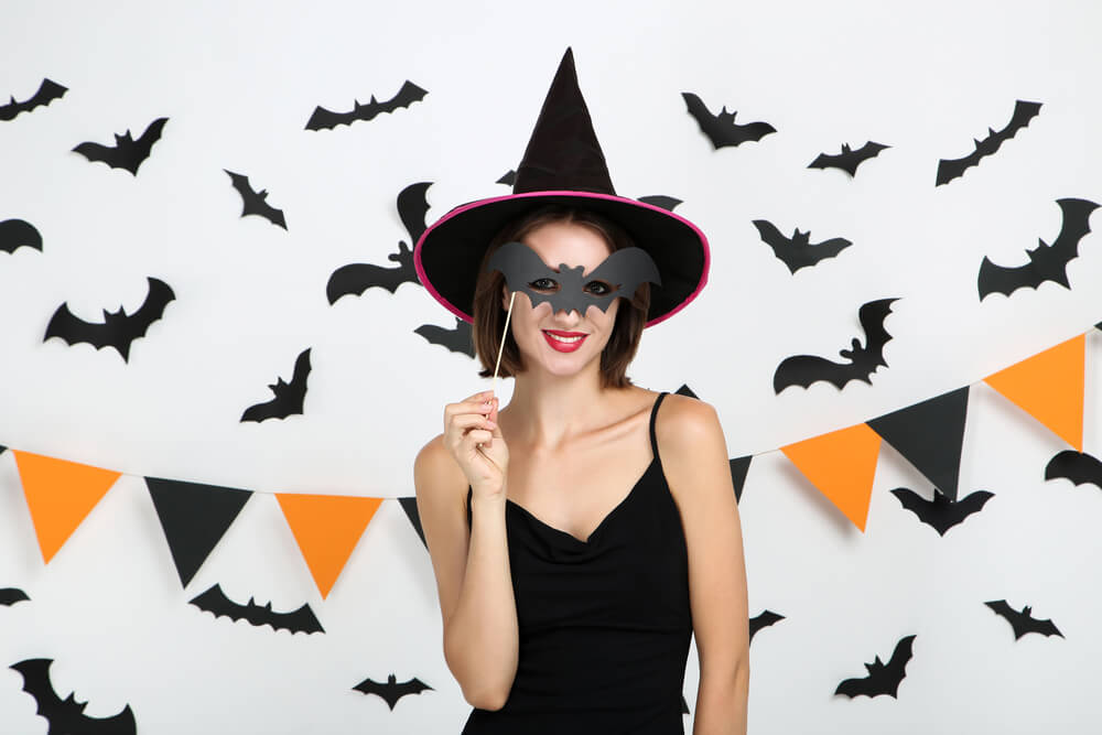 lady dressed as a witch standing in front of backdrop of paper bat cut outs