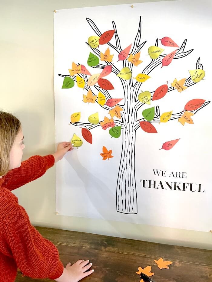 girl putting leaves on a wall sized Thankful tree