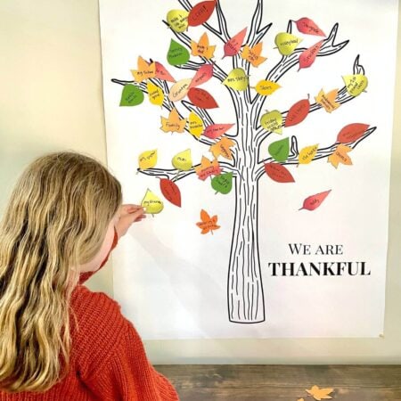 girl putting a paper leaf on a thankful tree