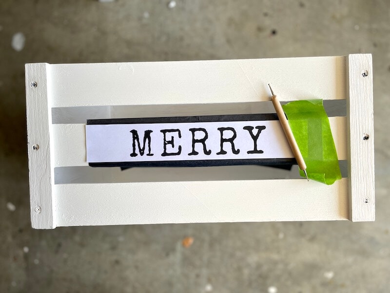 stenciling merry on a white wood crate