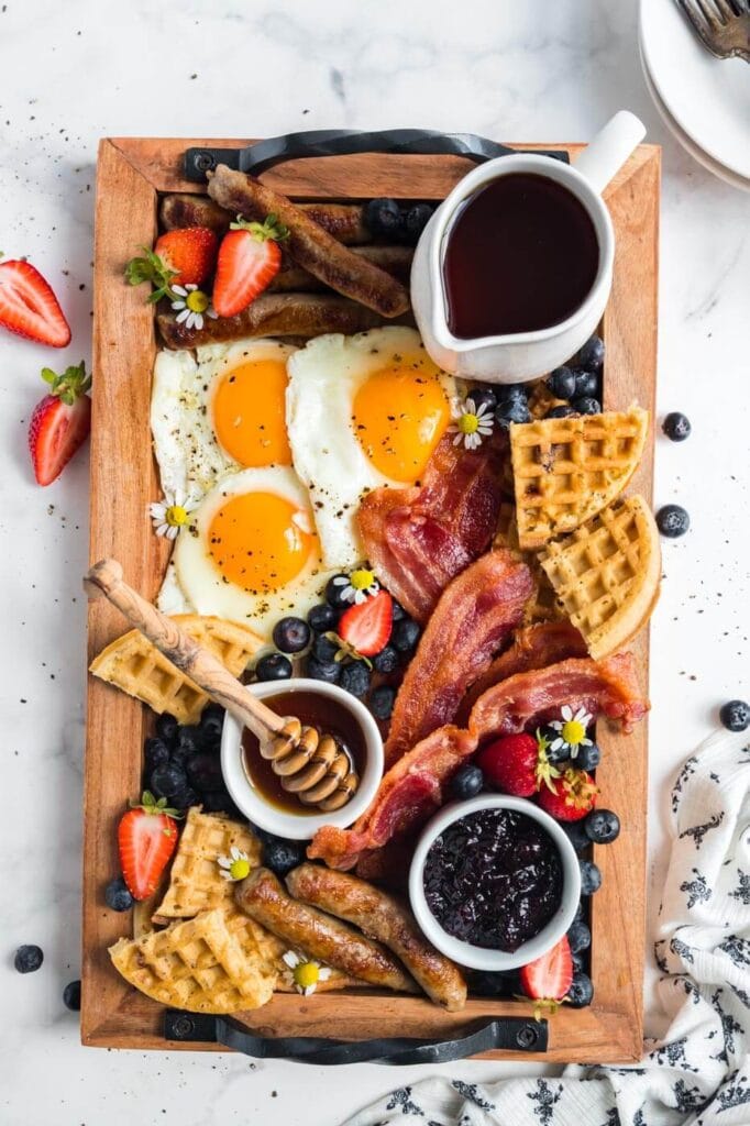 breakfast charcuterie board with waffles, jams, fruits, and breakfast meats