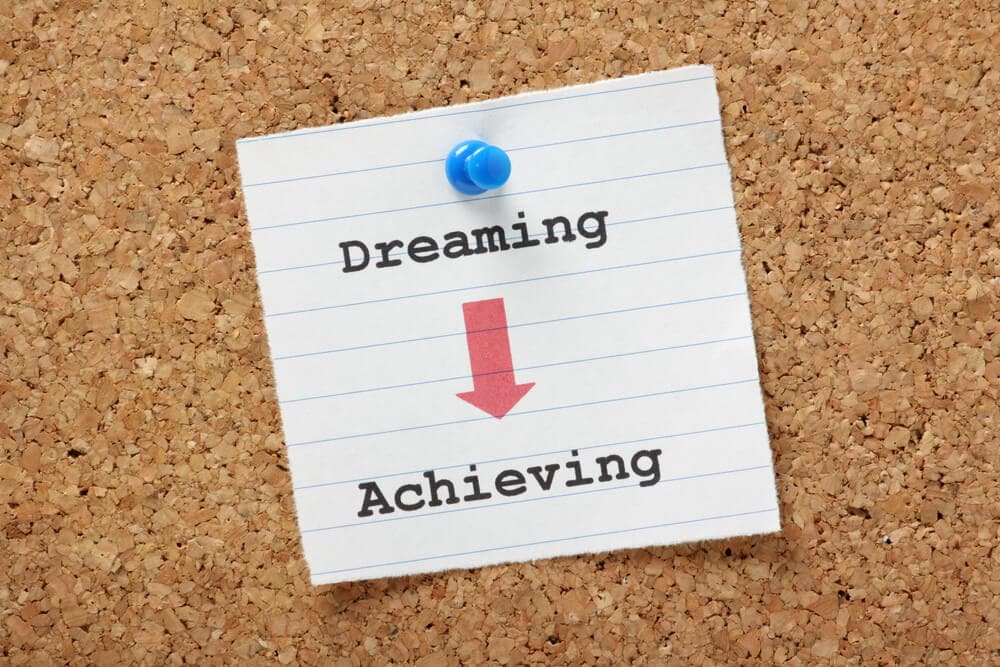 note on a bulletin board that says dreaming to achieving