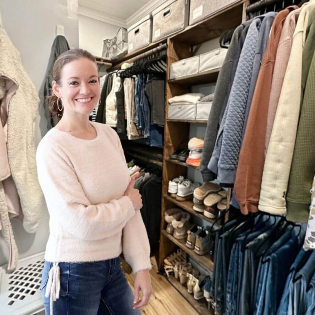 woman standing in an organized closet with color coordinated hanging clothes